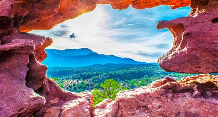 Breathtaking Colorado Red Rocks formation with dramatic mountain vista through natural stone arch opening under blue sky