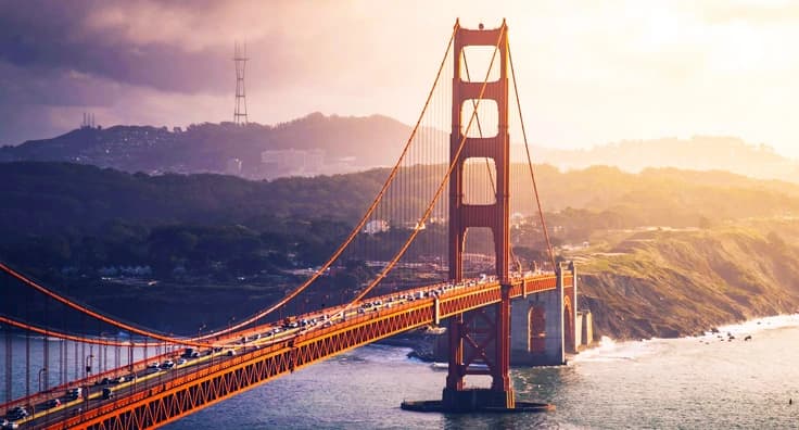 Iconic Golden Gate Bridge in San Francisco at sunrise with dramatic orange glow over Pacific Ocean and Marin Headlands